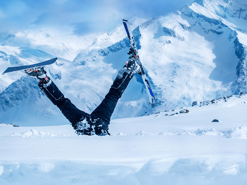 Das Bild zeigt eine Schipiste und einen Schifahrer, der kopfüber im Schnee steckt und die Schi noch an hat.